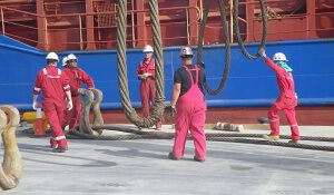 Arbeiter in roten Overals und mit Schutzhelmen an dicken Tauen