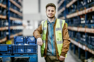 Portrait von Tim Zündorf auf blaue Kisten in einer Logistikhalle gelehnt